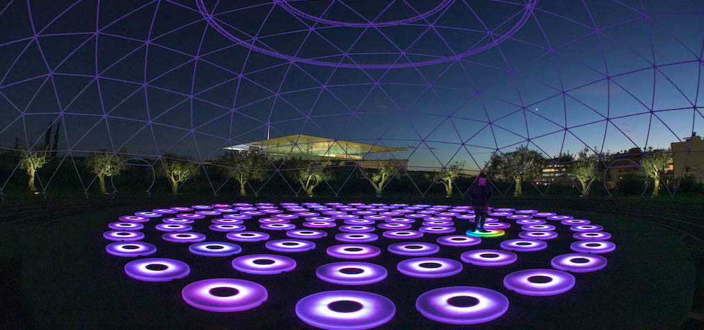 The Pool (2008, traveling) by Jen Lewin is an immersive interactive sculpture composed of mirrored hexagonal platforms laid flat like stepping stones. During the day, the surfaces reflect the sky and surroundings; at night, embedded LEDs respond to touch and movement, creating waves of color across the surface. The work invites users to walk, interact, and explore as their motion triggers light choreography, merging reflective geometry, playful interaction, and communal engagement. The sculpture has appeared at numerous international events, including light festivals, public plazas, and art fairs.